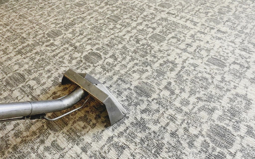 Steam wand cleaning a grey patterned area rug