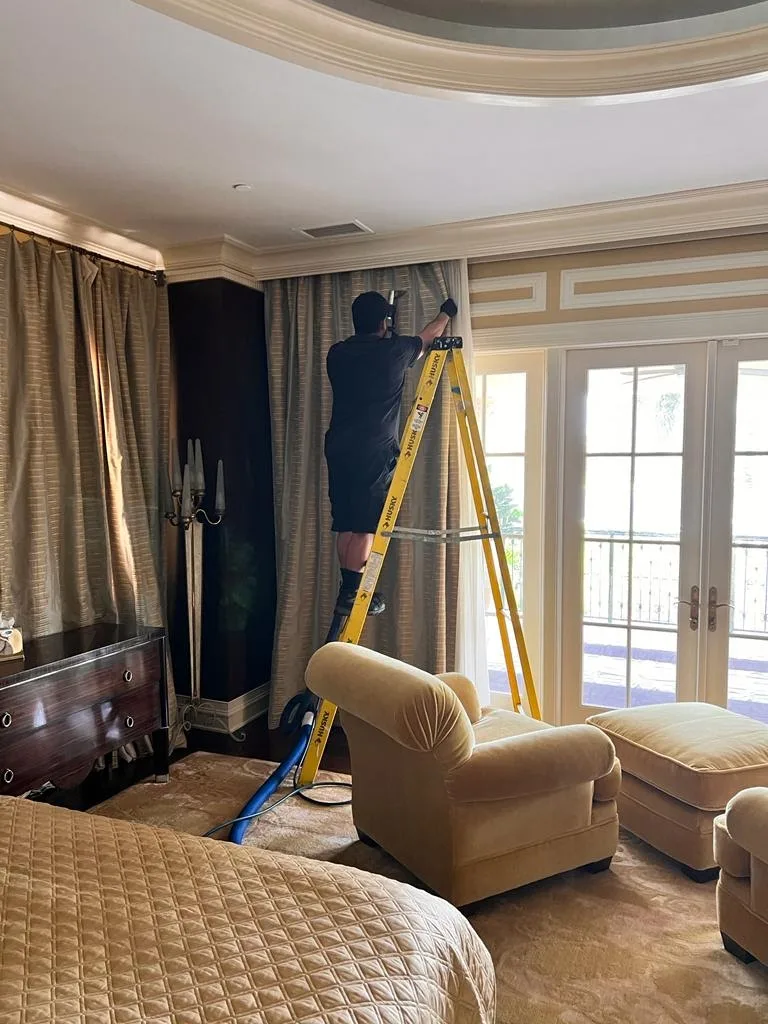 Technician on a ladder steam-cleaning bedroom drapes in place